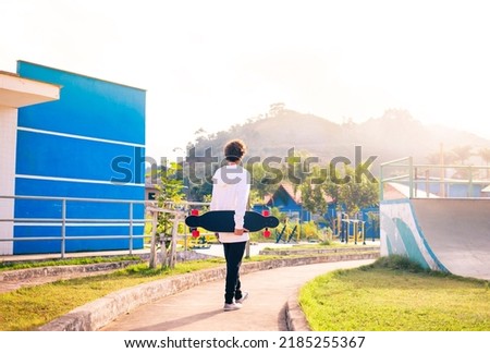 Young man holding a longboard at the skate park with sunset in the background.