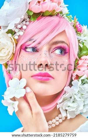 Spring and summer beauty. Portrait of a pretty teen girl with bright pink make-up posing in colored pink wig and flower wreath on head. Studio portrait on a blue background.