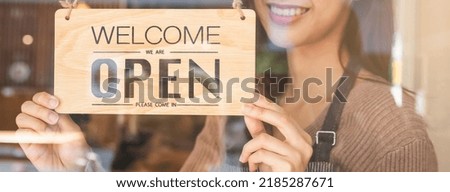 Smiling young asian woman owner, employee retail coffee shop woman hand in turning, setting sign board to open for welcome customer, reopen store after close lockdown quarantine in covid.Label concept