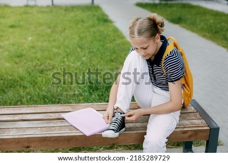 A cute teenage girl is sitting on a bench and tying her shoelaces