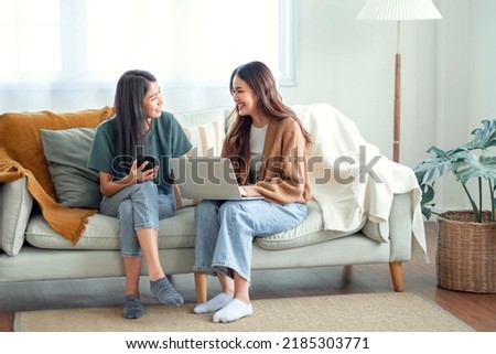 Two woman communicate with their friends and classmates via video link using a laptop and smartphone in the living room. Friends, friendship, time together Royalty-Free Stock Photo #2185303771