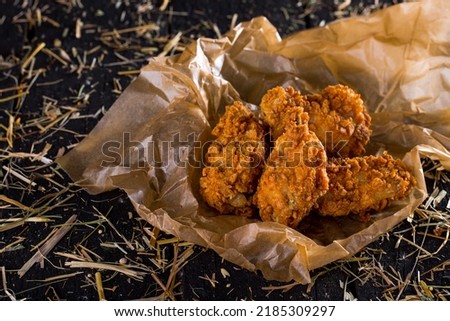 Fried chicken legs, breaded on parchment paper and black straw background. Horizontal orientation