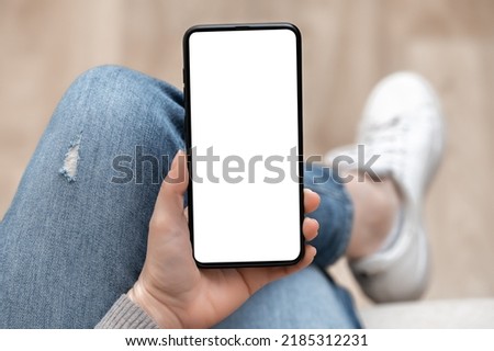 Top view mockup image of woman holding mobile phone with blank white screen. woman using cellphone with while sitting cross-legged on sofa at home. Mockup smartphone