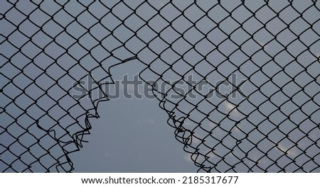 Opening in metallic fence against a blue sky with white clouds. Challenge. uncertainty. breakthrough concept. metaphor. Chain-link, wire netting, wire-mesh, cyclone hurricane fence