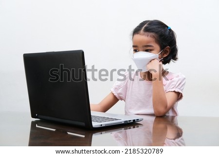 Asian little girl wearing medical mask joining online school from home