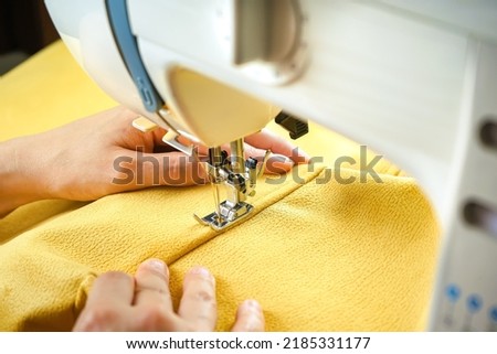 Seamstress female hands holding and stitching yellow textile fabric on modern sewing machine at workplace. Sewing process, upholstery, clothes, repair, DIY. Handmade, hobby, small business concept Royalty-Free Stock Photo #2185331177