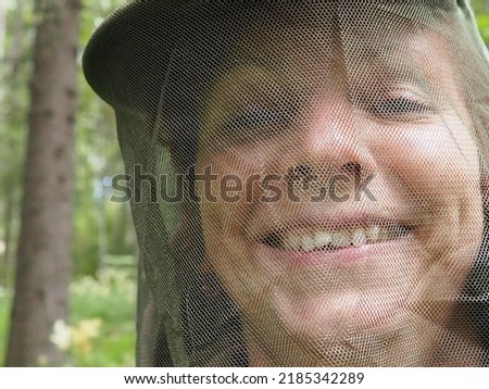 A woman in her 40s wearing a mosquito headdress smiles and looks at the camera. Cap and mesh against insects, mosquitoes, bees, wasps. Hunting and fishing in the spruce forest. Royalty-Free Stock Photo #2185342289