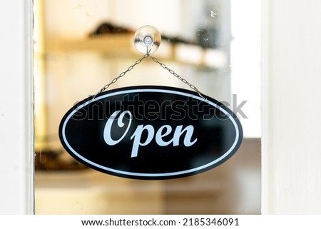 Shop door oval open sign hanging on glass entrance to retail business interior blurred in background