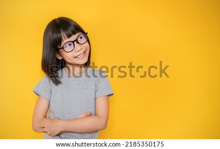 Portrait of young happy nerd little asian girl in gray t shirt looking isolated on yellow background copy space. Education for nerdy toddler or preschool, childhood lifestyle back to school concept