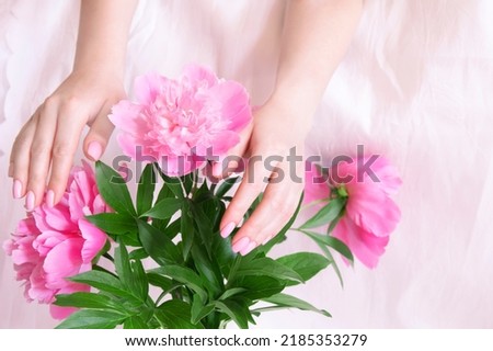 Woman hands close up touching a pink peony on a white background.