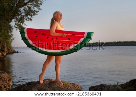 Summer lifestyle portrait senior woman in swimwear with air mattress looks like watermelon on the seashore. Enjoying the little things. spends time in nature in summer
