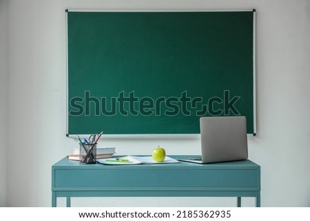 Apple with books, pen cup and laptop on table near school chalkboard