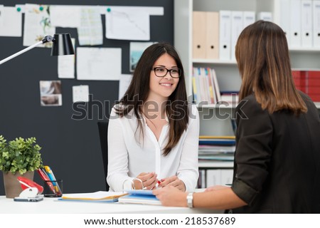 Two young businesswomen having a meeting in the office sitting at a desk having a discussion with focus to a young woman wearing glasses Royalty-Free Stock Photo #218537689