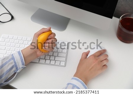 Woman squeezing antistress ball while working on computer in office, closeup Royalty-Free Stock Photo #2185377411