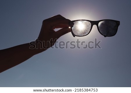 creative photo on the background of blue sky and sunset a girl in her hands holds sunglasses directly above the sun.Summer concept beautiful nature screensaver