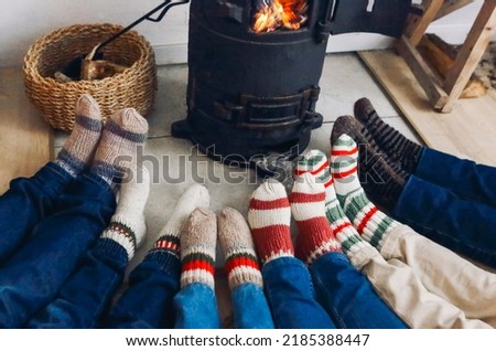 Cropped photo of big family wearing warm woolen socks resting by fireplace together in winter time. Mother, father and children lying on floor warming feet near potbelly stove in country house Royalty-Free Stock Photo #2185388447