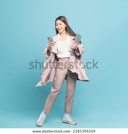 Young beautiful asian woman with smart casual cloth wearing pink coat smiling holding smartphone and laptop isolated on blue background Royalty-Free Stock Photo #2185396569