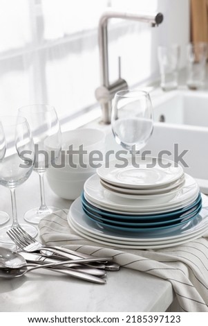Different clean dishware, cutlery and glasses on countertop near sink in kitchen Royalty-Free Stock Photo #2185397123