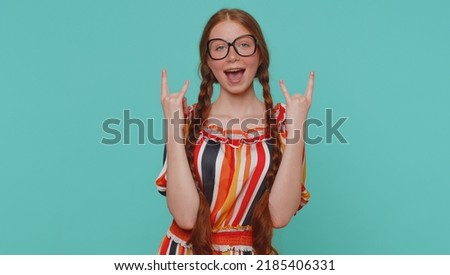 Rock n roll. Overjoyed delighted redhead girl in dress showing gesture by hands, cool sign, shouting yeah with crazy expression, dancing, emotionally rejoicing in success win alone on blue background