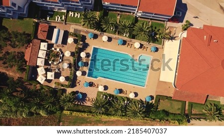 Top view of a small hotel pool with white and blue umbrellas standing nearby. Place ready for tourists and travelers from across the world. High quality photo