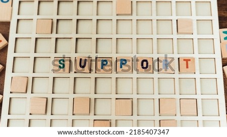 Support. Word puzzles concept. Square cube colourful letters on a wooden board seen from above. High quality photo