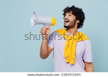 Promoter jubilant young bearded Indian man 20s years old wears white t-shirt hold scream in megaphone announces discounts sale Hurry up isolated on plain pastel light blue background studio portrait Royalty-Free Stock Photo #2185415693