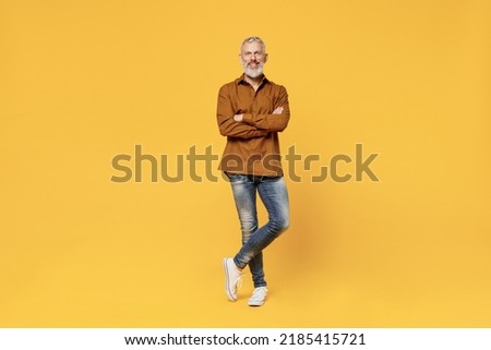 Full size body length excited charismatic elderly gray-haired bearded man 40s years old wears brown shirt looking camera smiling keep hands crossed isolated on plain yellow background studio portrait Royalty-Free Stock Photo #2185415721