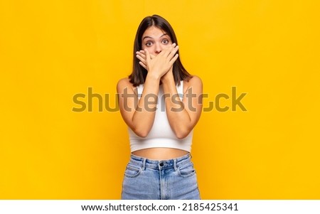 young pretty woman covering mouth with hands with a shocked, surprised expression, keeping a secret or saying oops