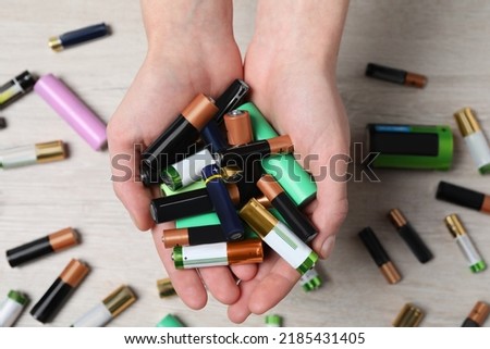 Woman holding many used electric batteries in her hands over white table, closeup Royalty-Free Stock Photo #2185431405