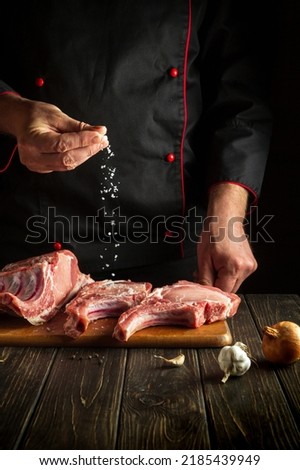 Chef sprinkles raw ribs with salt. The concept of cooking delicious food for the hotel or restaurant Royalty-Free Stock Photo #2185439949