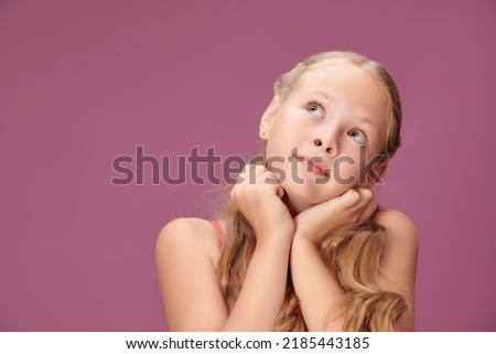 A pretty blonde girl with wavy hair looks dreamily up. Studio shot on a purple background. Children's summer fashion. Copy space.