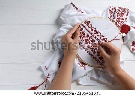 Woman embroidering shirt with red thread at white wooden table, top view and space for text. Ukrainian national clothes Royalty-Free Stock Photo #2185451339