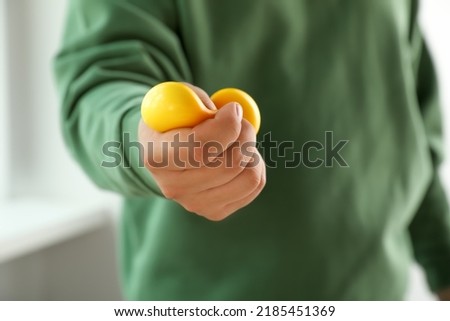 Man squeezing yellow stress ball indoors, closeup Royalty-Free Stock Photo #2185451369