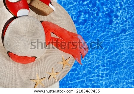 Women's hat, sandals and starfish next to the pool. Red beautiful sandals and straw on a background of blue water