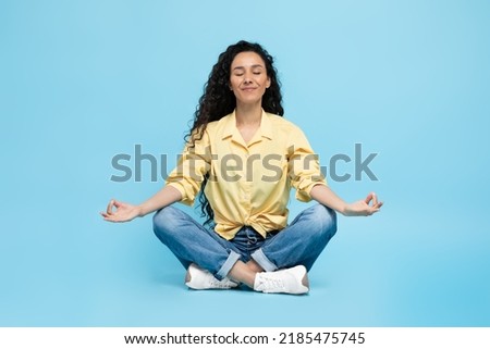 Mindfulness. Calm Arabic Woman Meditating Sitting In Lotus Position Doing Om Gesture Relaxing Over Blue Studio Background. Yoga Exercise And Meditation Concept Royalty-Free Stock Photo #2185475745