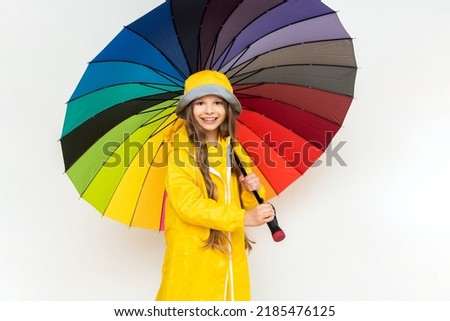 A child with a colorful umbrella in a yellow raincoat and a panama hat on a white isolated background.