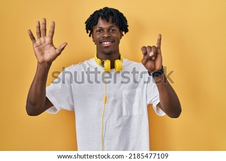 Young african man with dreadlocks standing over yellow background showing and pointing up with fingers number six while smiling confident and happy. 