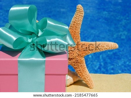 Gift box and a large starfish on the background of the pool. The pink box is decorated with a green ribbon on a background of turquoise water.