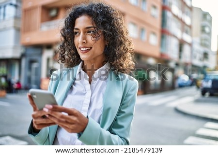 Young hispanic business woman wearing professional look smiling confident at the city using smartphone Royalty-Free Stock Photo #2185479139