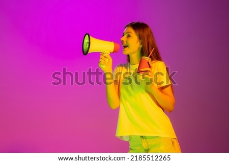 Portrait of young cheerful girl posing, shouting in megaphone isolated over pink background in neon light. Concept of beauty, style, lifestyle, youth, emotions, facial expression. Copy space for ad