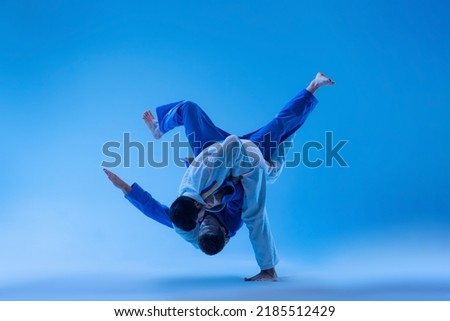 One-arm shoulder throw. Dynamic portrait of professional judo athletes training isolated over blue studio background in neon light. Concept of martial art, combat sport, health, strength, energy, fit. Royalty-Free Stock Photo #2185512429