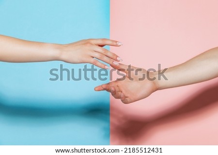 Image of male and female hands reaching each other isolated over pink blue studio background. Support. Concept of youth, emotions, facial expression, love, relationship. Poster, ad