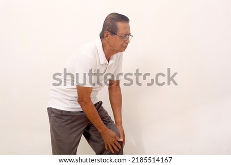 Elderly asian man suffering from knee pain. Isolated on white background with copyspace Royalty-Free Stock Photo #2185514167