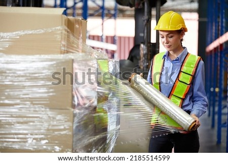 factory worker or warehouser wrapping stretch film parcel on pallet covered cardboard boxed in warehouse storage