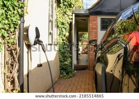 Electric car plugged in to charge outside home with power cable Royalty-Free Stock Photo #2185514865