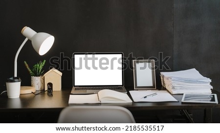 Modern office with laptop computer and office supplies on desk with dark wall background.