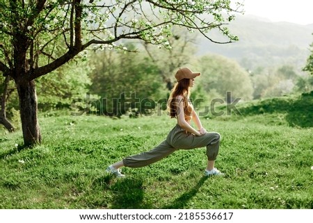 A young athletic woman does sports stretching in nature in the park. Green summer landscape in the sunlight in nature