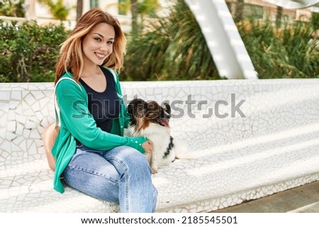 Young caucasian girl smiling happy sitting on the bench with dog at the city.