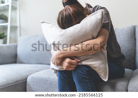 Unhappy anxiety young Asian woman covering her face with pillow on the cough in the living room at home. Royalty-Free Stock Photo #2185566125