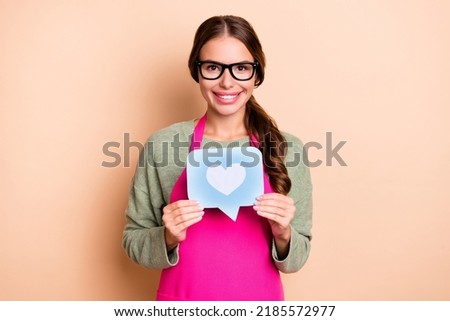 Photo of cheerful charming girl dressed pink apron eyewear rising heart like sign isolated beige color background
